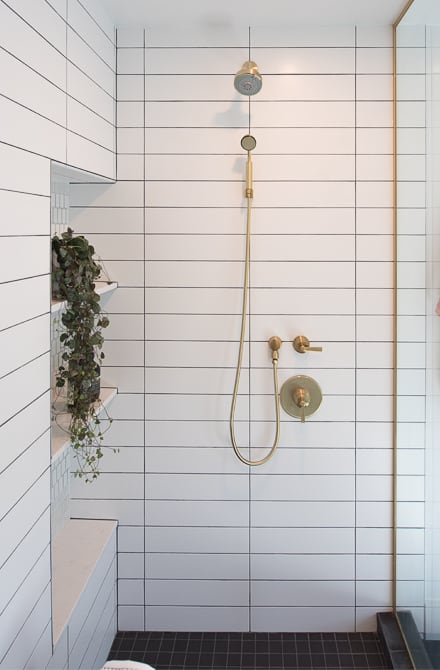 Perfectly precise white rectangular tiled shower with gold fixtures and built-in niche