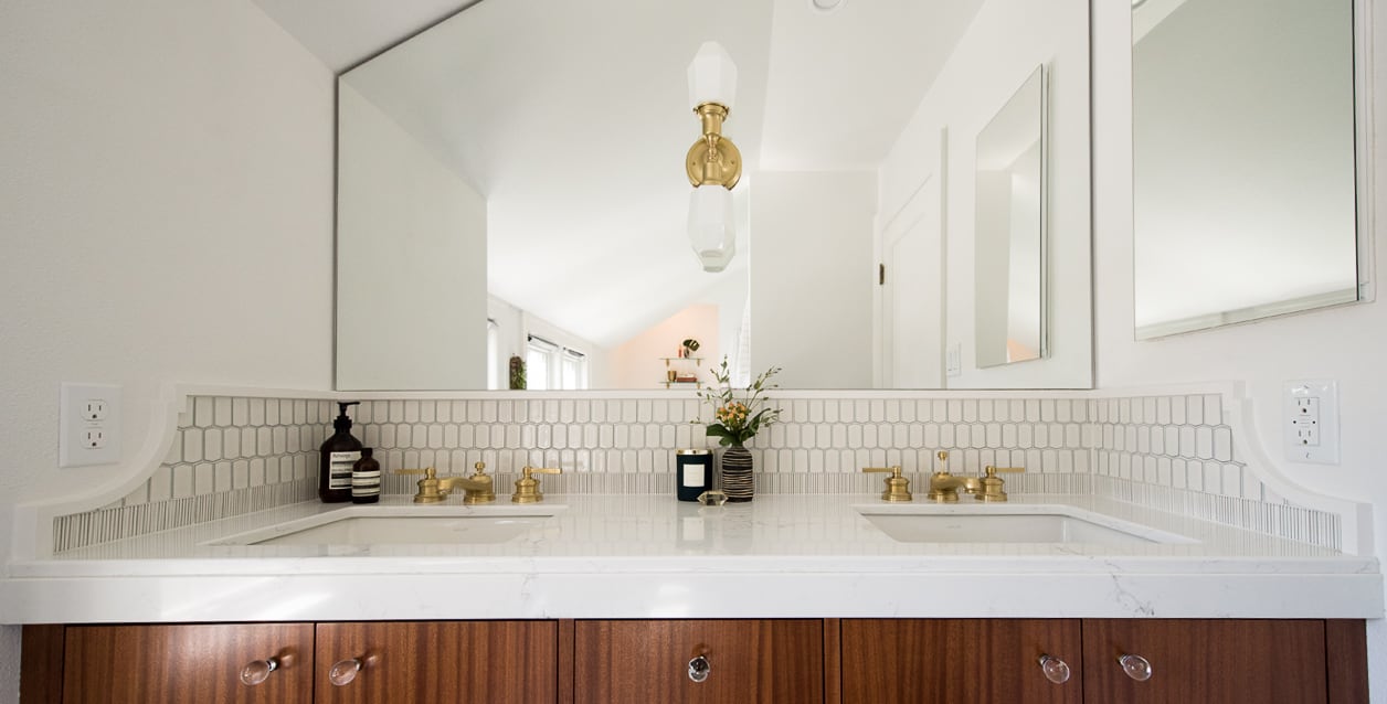 Detail of double bathroom sink with gold fixtures, gold sconce and mahogany cabinet