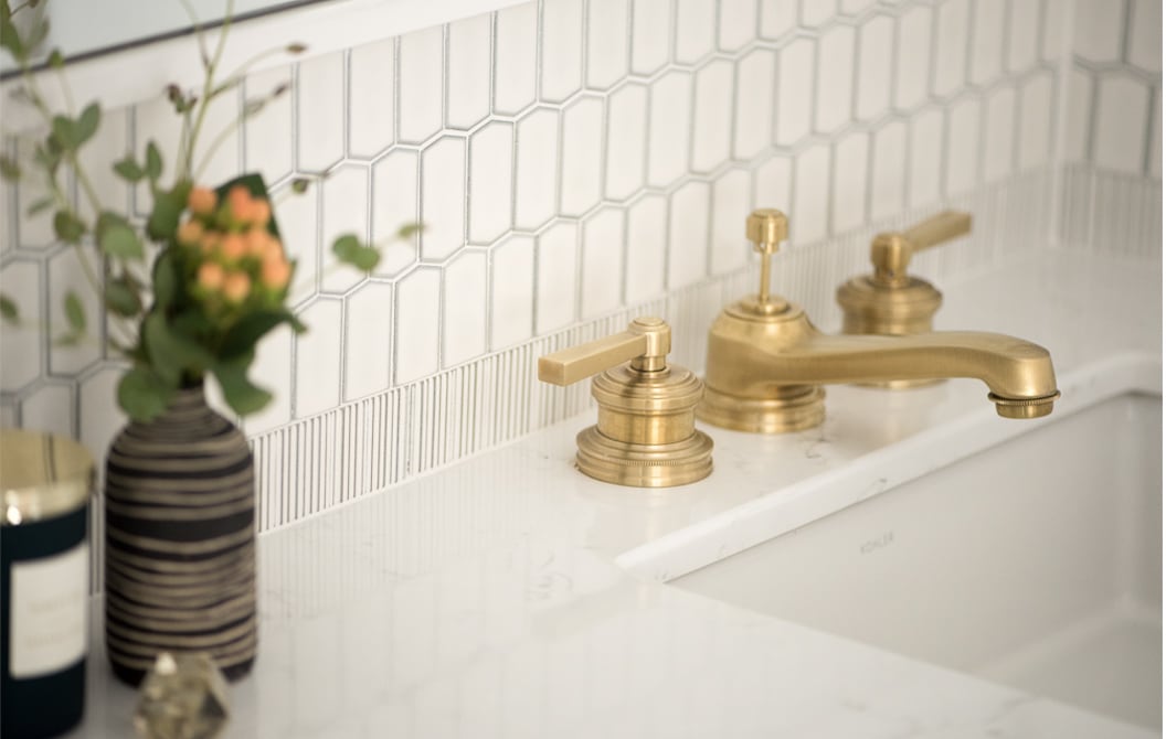 Detail of brushed gold faucet fixture and cream kit-kat tile backplash