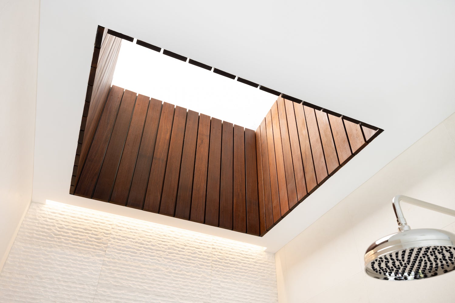 View looking up at ceiling with skylight trimmed in vertical mahogany slats above shower