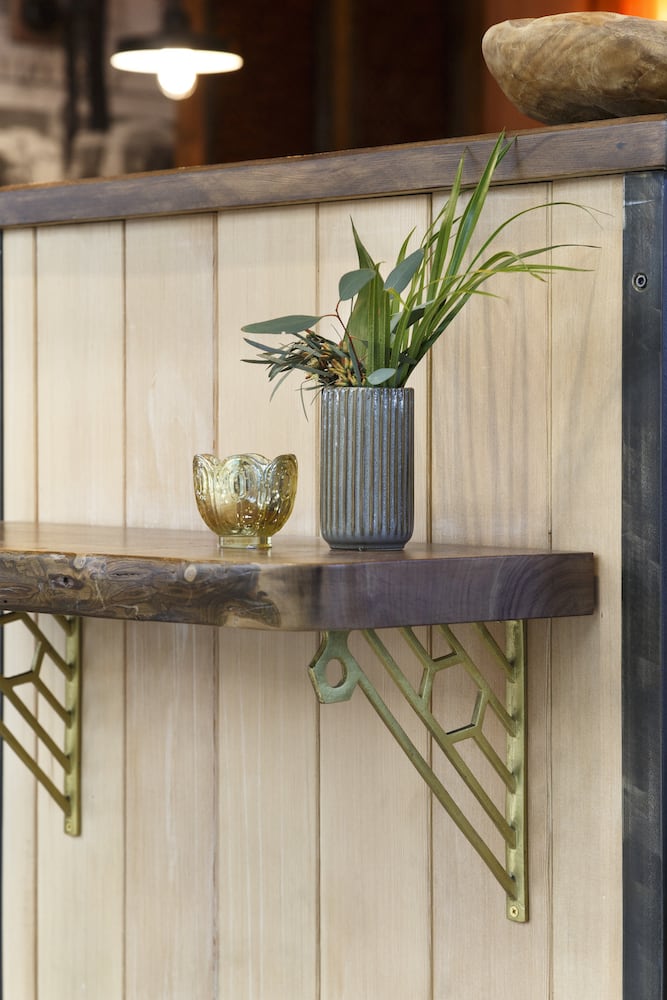 Detail of live-edge shelf holding a plant with vintage reclaimed gold angle brackets