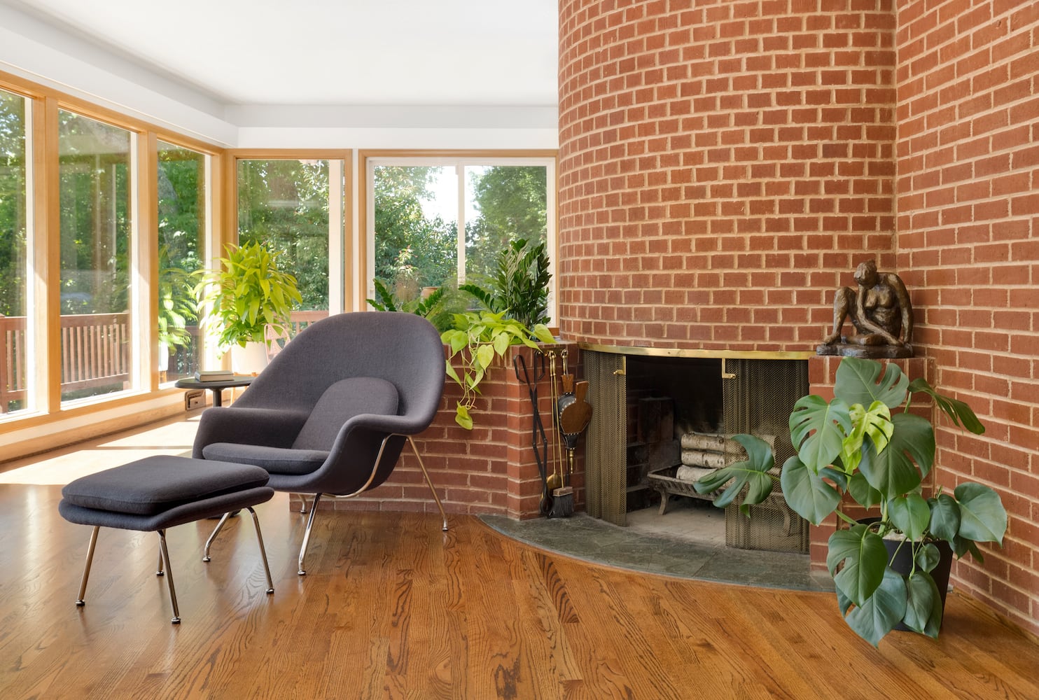 Brick circular fireplace with built-in planter, floor to ceiling windows, womb chair