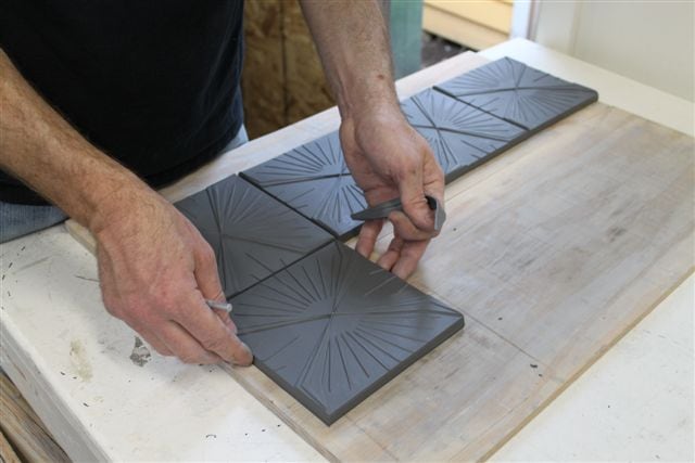 Person using tools to create modern designs on charcoal colored ceramic tiles
