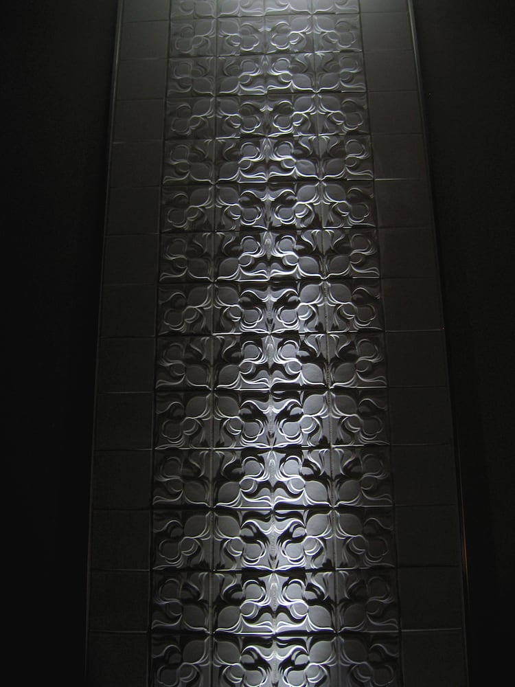 Light shining up a dark wall of white textured tile, throwing beautiful shadows