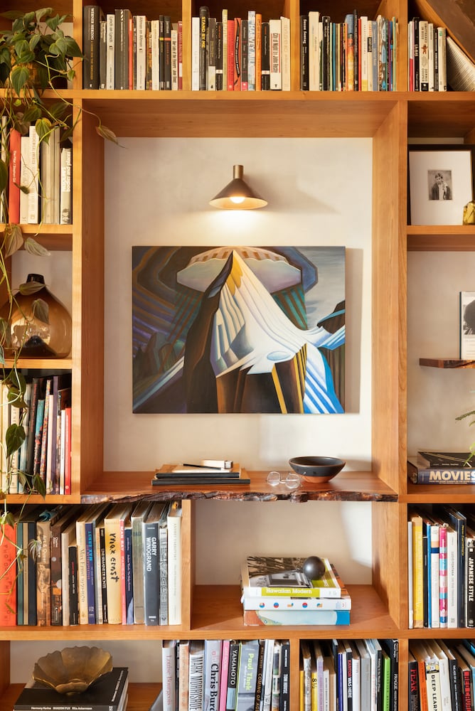 Artwork hangs with modern lighting among a custom cherry bookshelf system