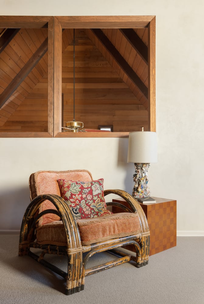 A vintage cushioned wood recliner chair sits in front of open aired indoor balcony windows