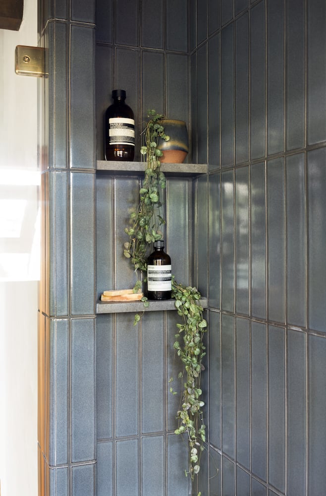 Two shower niche shelves are created out of blue tile for soaps and hanging plants