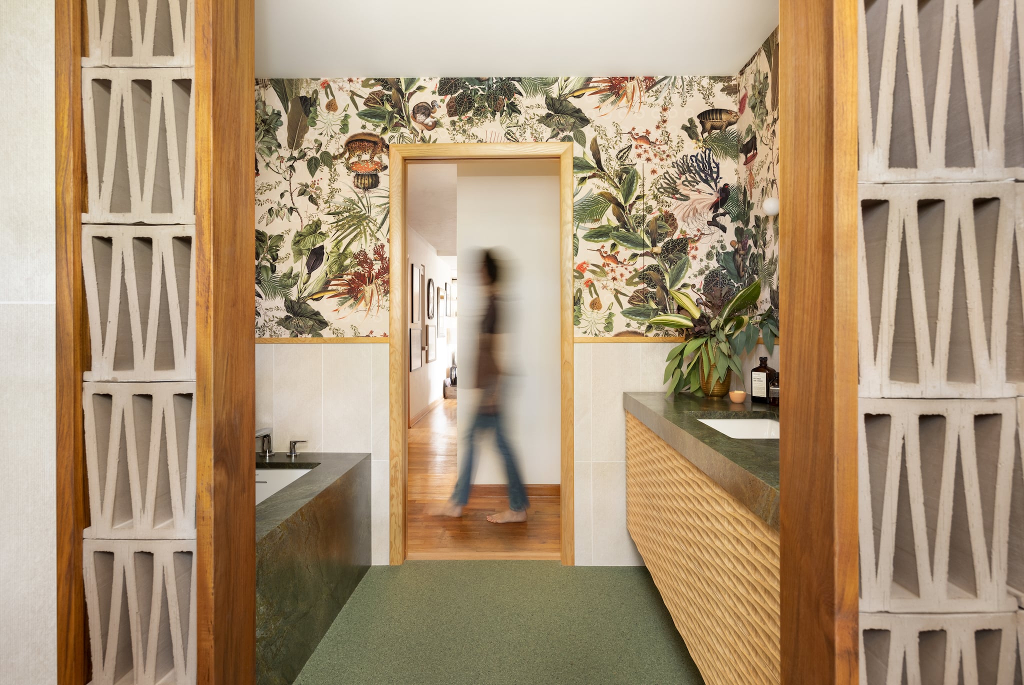 A person in the hallway walks past this tropical green bathroom remodel