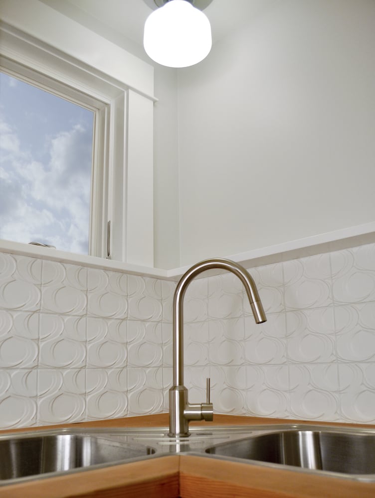 Detail of polished silver dual-sink with wood countertops, white tile backsplash
