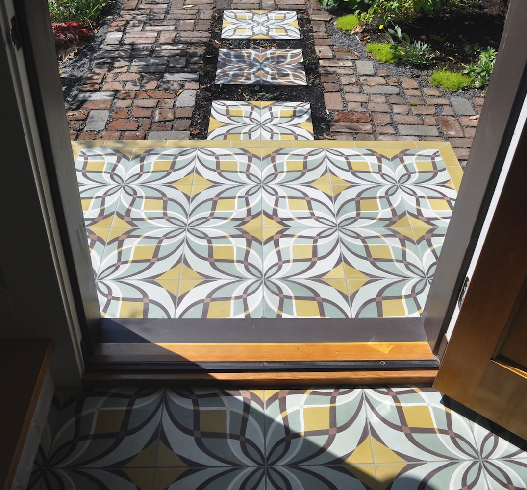 Sunlight shines on front step's patterned hydraulic cement pressed tile, brick