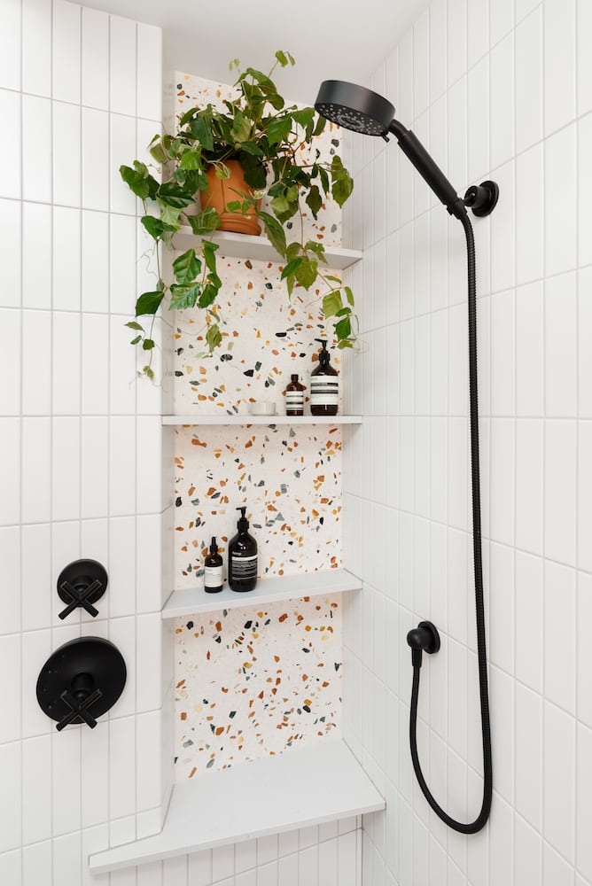 Residential terrazzo shower niche with black plumbing fixtures, white tile