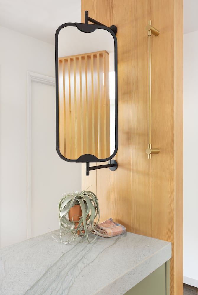 Modern designed lighting fixture and swivel mirror hang from a wood wall above quartz
