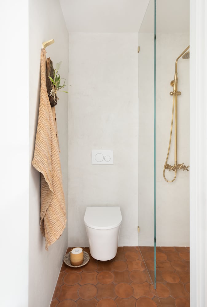 A small bathroom with a wallhung toilet and glass pane shower, tierra tile flooring