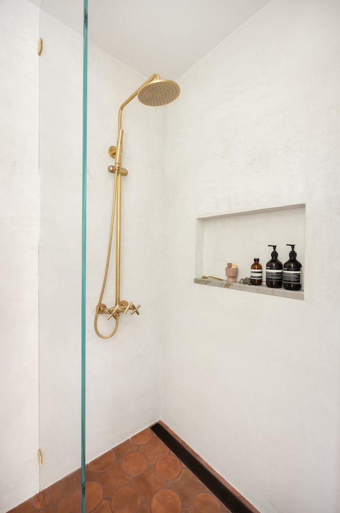 Glass pane shower with gold showerhead and linear drain among mexican floor tile