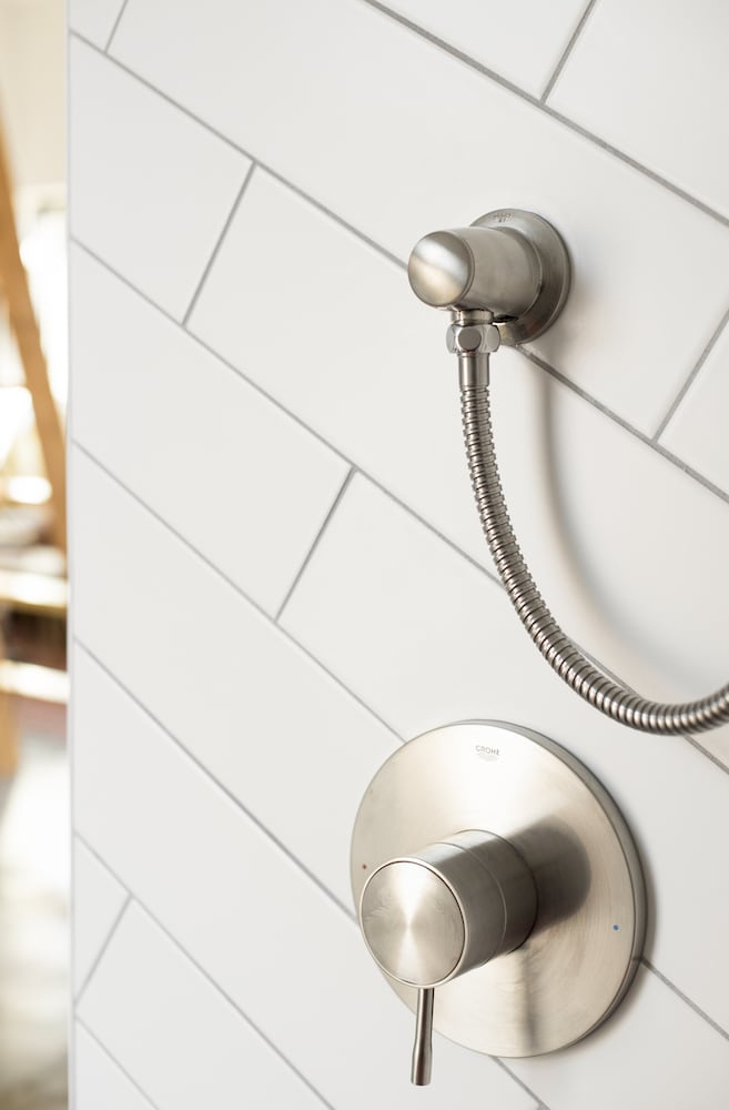 Detail of brushed Grohe hand shower handle and hose with white diagonal tile