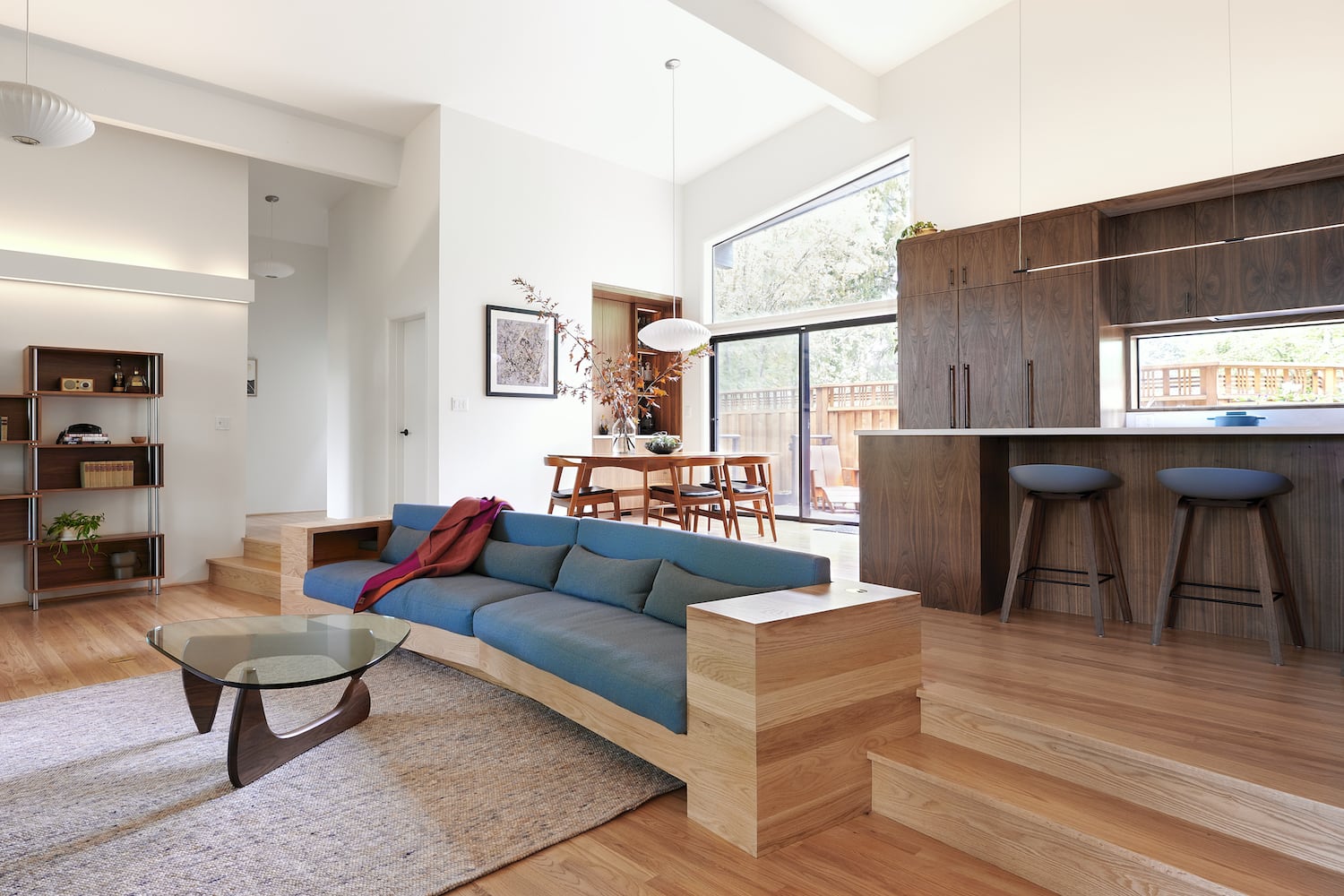 Midcentury living space with built-in sofa, indirect soffit lighting, wood floor