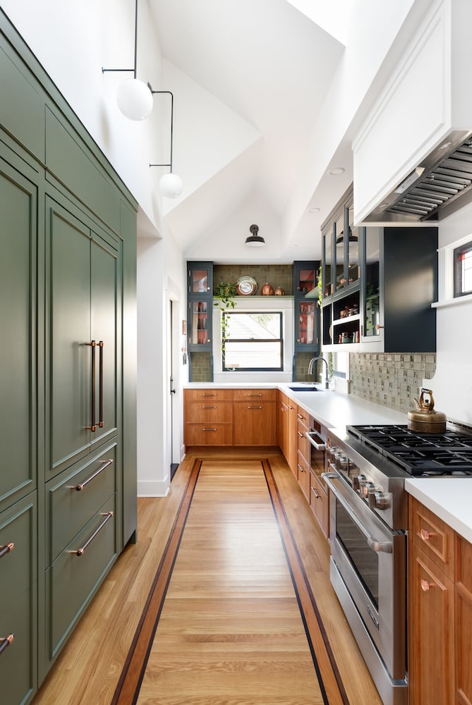 Kitchen with wood floors, cherry and green cabinets, glass front cabinets, wall sconces