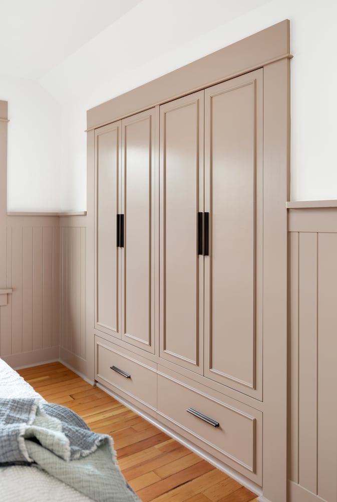 Primary bedrom built-in closet with painted cabinets and wainscot