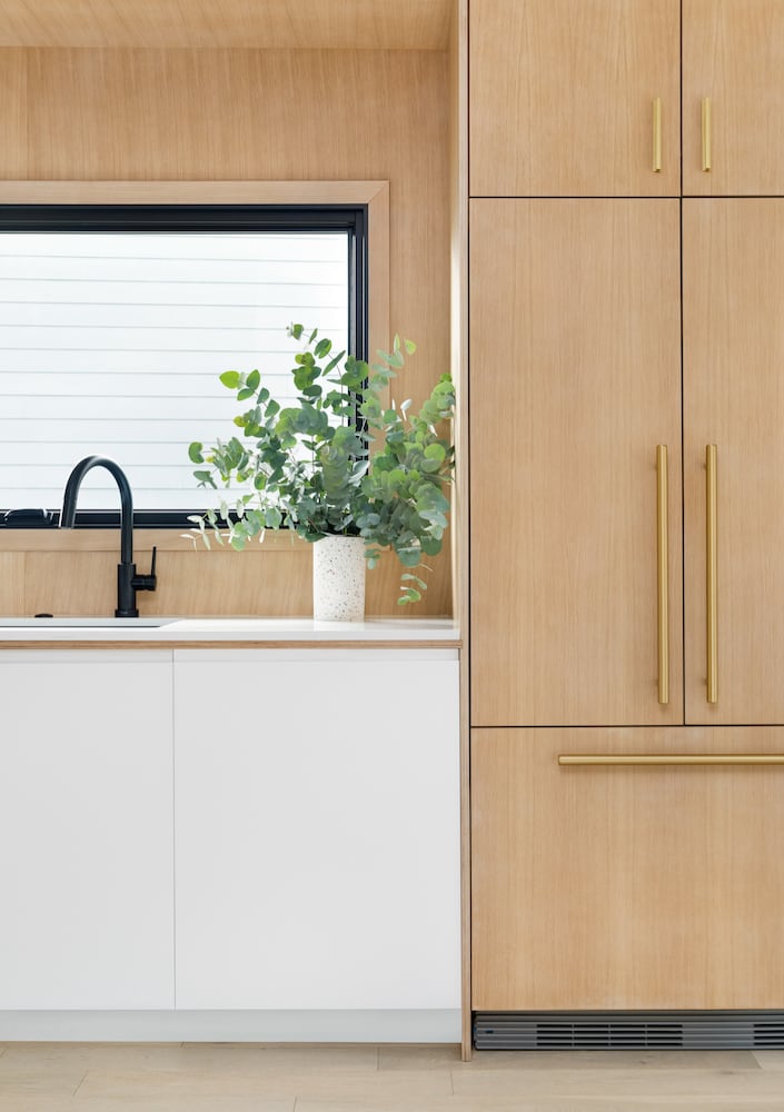 Modern kitchen, light wood panel front fridge, white base cabinets, black window