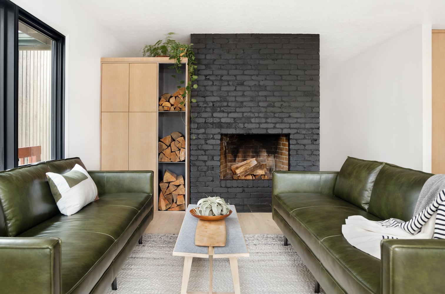 Modern house living room with green leather sofas, black fireplace, firewood storage