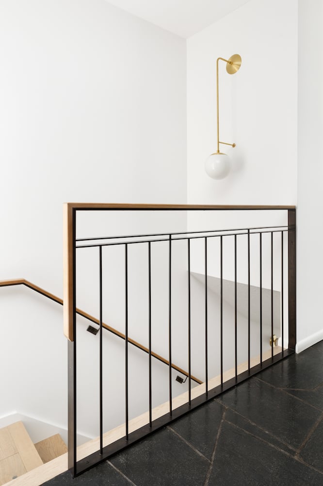 Modern minimal stairwell with custom steel and wood railing, gold wall sconce