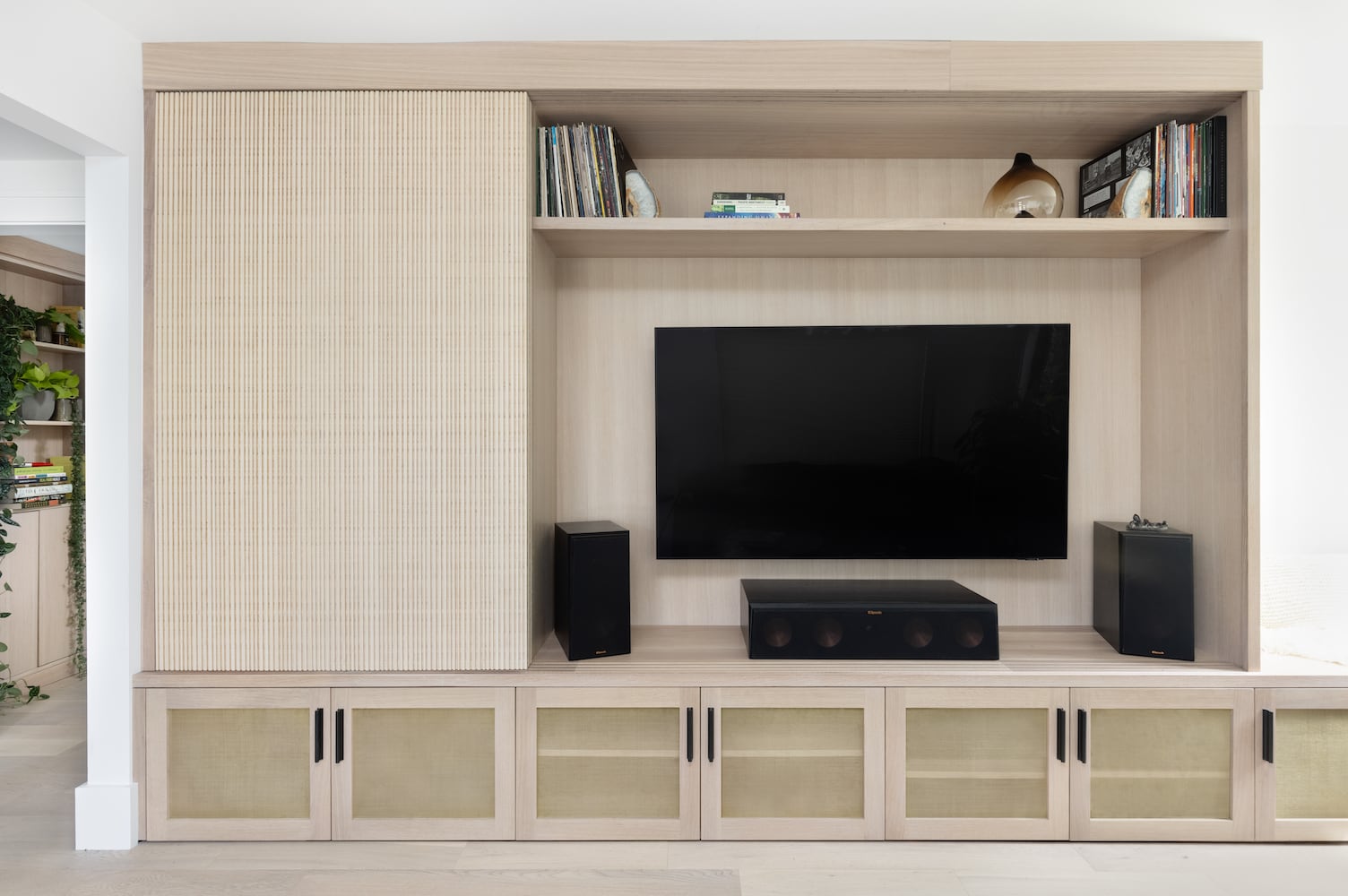 Custom white oak casework revealing entertainment system with gold mesh paneling below