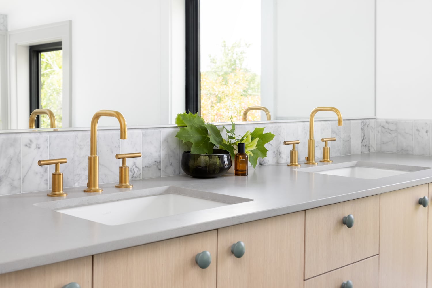 Detail of double sinks with polished gold fixtures, earth green cabinet pulls