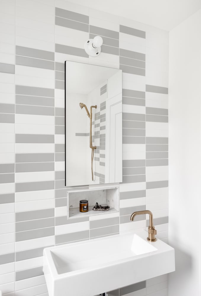 Bathroom remodel with grey and white wall tile pattern, gold fixtures, marble niche