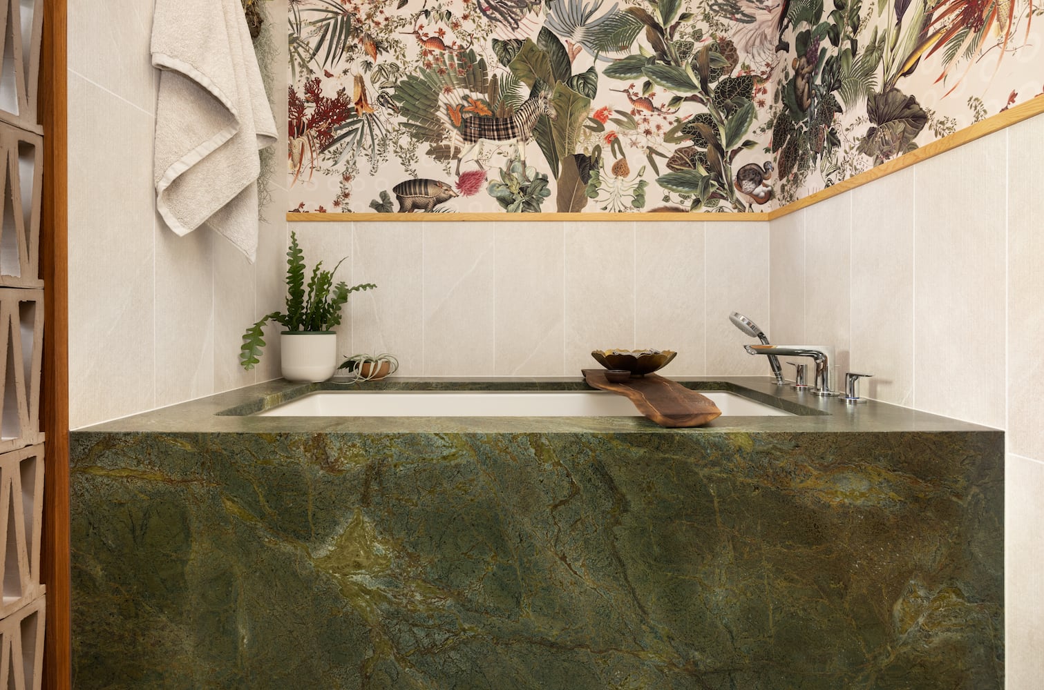 Bold style conveyed by green granite slab surrounding bathtub with vanilla tile backplash