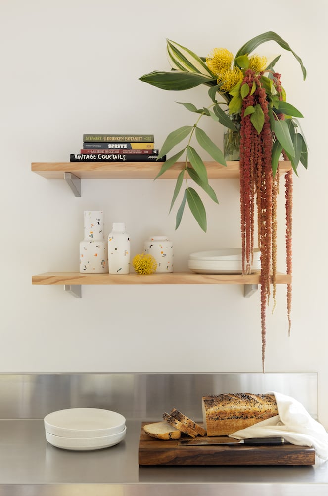 Above a stainless countertop with sliced bread hang a tropical plant, colorful ceramics