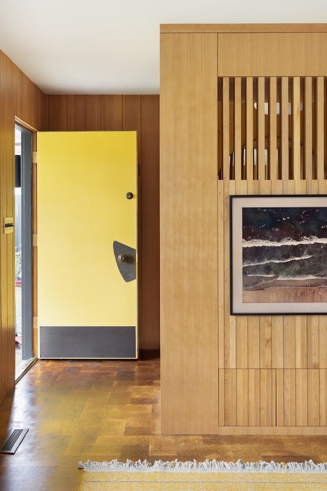Foyer of midcentury home with yellow front door opened and nautral light streaming in
