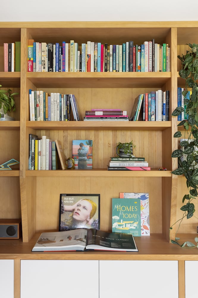 Detail of natural wood bookshelves, plants, white cupboards and David Bowie record